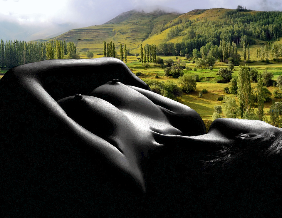 A nude woman in black & white on her back, her head turned towards the lush greens of a Greek mountain landscape background.